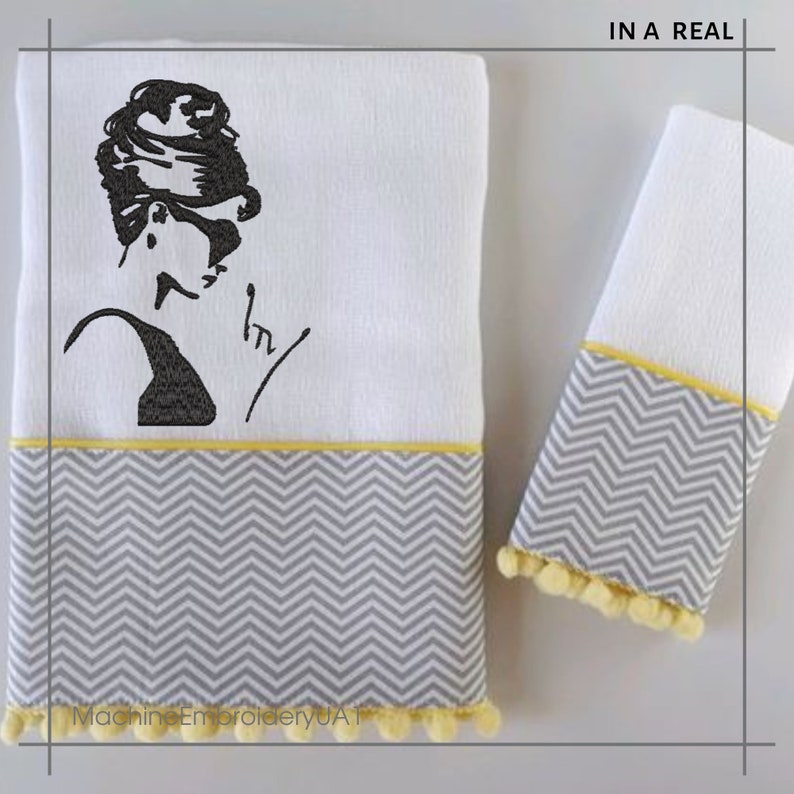 May include: Two white towels with gray and yellow chevron trim and pom-poms. One towel features an embroidered image of a woman with a bouffant hairstyle and sunglasses. The text "IN A REAL" is printed on the top right corner of the image.