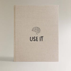 Może przedstawiać: Beżowy notatnik z ilustracją m&oacute;zgu i czarnym napisem "USE IT". Notatnik ma teksturowaną okładkę i minimalistyczny design.