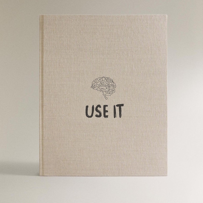 Może przedstawiać: Beżowy notatnik z ilustracją m&oacute;zgu i czarnym napisem "USE IT". Notatnik ma teksturowaną okładkę i minimalistyczny design.