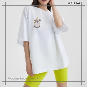 May include: White oversized t-shirt with a cartoon embroidery of The Little Prince on a planet with a fox. The text "IN A REAL" is in the top right corner of the image.