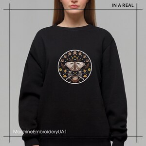 May include: Black sweatshirt featuring a circular design with a butterfly, moon phases, and floral elements. The text "IN A REAL" is at the top right. The text "MachineEmbroideryUA1" is at the bottom left.