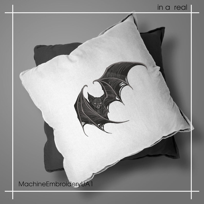 May include: A white square throw pillow featuring a detailed black embroidered bat with spread wings, layered over a solid black square pillow. The text "in a real" appears in the top right corner and "MachineEmbroideryUA1" in the bottom left.