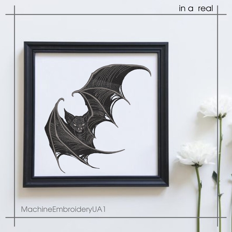 May include: A square black frame containing a white fabric panel with a detailed black machine embroidery design of a bat with spread wings. The text "in a real" appears in the top right corner and "MachineEmbroideryUA1" in the bottom left.