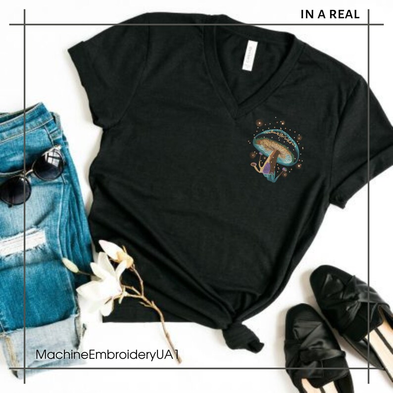 May include: Black v-neck t-shirt with a blue and purple mushroom graphic with gold glitter accents. The text "IN A REAL" is printed in white at the top of the shirt.