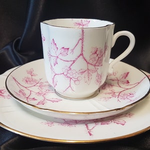 May include: A white teacup and saucer set with a pink floral design. The cup has a scalloped rim and a handle. The saucer has a gold trim.