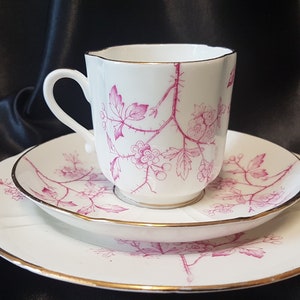 May include: A white teacup and saucer set with a pink floral design. The cup and saucer have a gold trim around the edge.