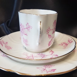 May include: A white teacup and saucer set with a pink floral pattern. The set has a gold trim around the edges.