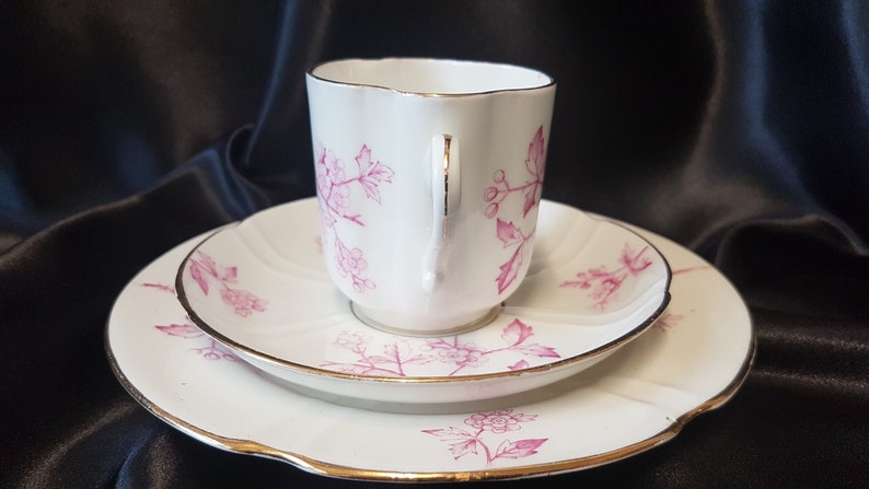 May include: A white teacup and saucer set with a pink floral pattern. The set has a gold trim around the edges.