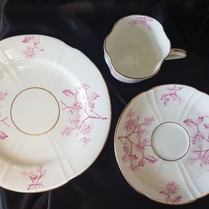 May include: A set of three white porcelain teacups and saucers with a pink floral design. The cups and saucers have a gold trim.