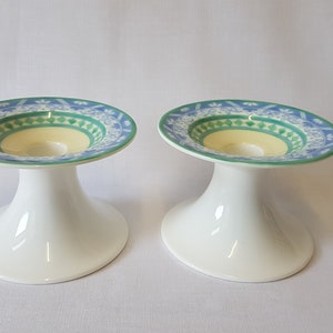 May include: Two white ceramic candle holders with a blue, green and yellow patterned design.