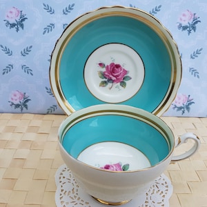 Puede incluir: Un juego de taza y platillo vintage con un diseño floral azul turquesa y blanco. La taza y el platillo tienen un borde dorado.