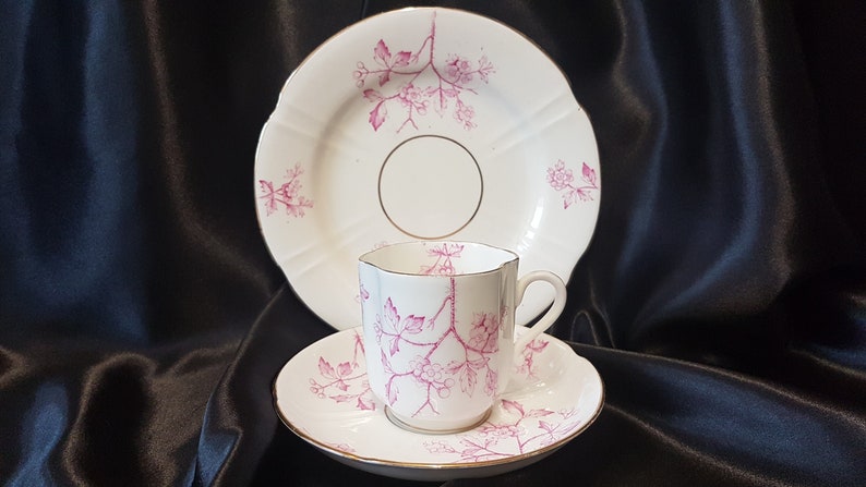 May include: A white teacup and saucer set with a pink floral pattern. The saucer has a scalloped edge and the cup has a delicate floral design.