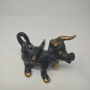 May include: Black ceramic bull figurine with gold accents. The bull has a curled tail, a gold horn, and gold accents on its hooves and neck.