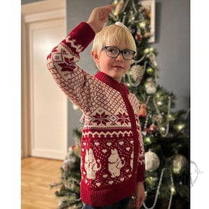 May include: A red and cream-colored zip-up sweater with a festive pattern. The sweater features a repeating geometric design on the sleeves and upper body, with a whimsical illustration of cartoon characters on the lower front. The sweater is worn by a child.