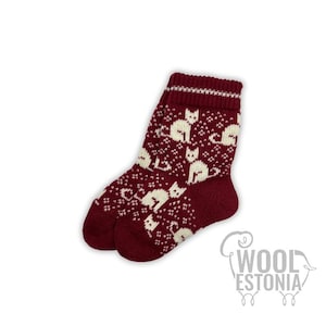 May include: A pair of burgundy wool socks with a white cat pattern. The socks have a ribbed cuff with a white stripe. The Wool Estonia logo is visible in the lower right corner.