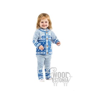 May include: A child's blue and white knit sweater and pants set. The sweater has a button-up front and a snowflake and geometric pattern. The pants have a matching pattern. The set is made of wool.
