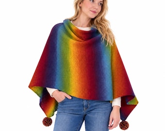 May include: A knitted poncho featuring a vibrant rainbow gradient pattern that transitions through shades of red, orange, yellow, green, blue, and purple. The garment has a high neckline and two decorative pom-poms attached at the bottom corners.