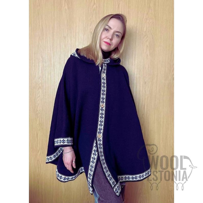 May include: A navy blue hooded cape with white and black trim. The cape has a button closure and is made of wool. The model is wearing the cape over a white shirt and jeans.