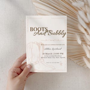 Puede incluir: Una invitación beige claro con el texto "BOOTS And Bubbly" y un dibujo de una bota de vaquero. La invitación incluye detalles para una celebración nupcial, incluyendo la fecha, hora y lugar.