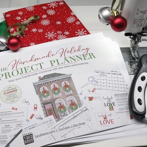 Printed Handmade Holiday Project Planner beside a sewing machine, rotary cutter, Christmas fabric, and jingle bells, ready for planning handmade holiday gifts.
