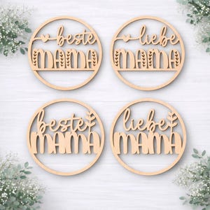 K&ouml;nnte beinhalten: Vier runde Holzdekorationen mit den Worten "beste MAMA" und "liebe MAMA" in einer Schriftart ausgeschnitten. Jeder Kreis hat einen dekorativen Rand und ein Herz- oder Blattdesign. Das Holz ist hell und nat&uuml;rlich.