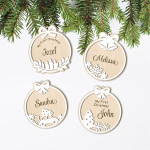 May include: Four wooden Christmas baubles with personalised names. Each bauble features a different design, including a wreath, a snowflake, a car with a Christmas tree, and a Christmas tree with snowflakes. The baubles are all white with brown text.