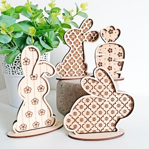 May include: Four wooden Easter bunny decorations with different floral patterns. The bunnies are standing on a white surface.