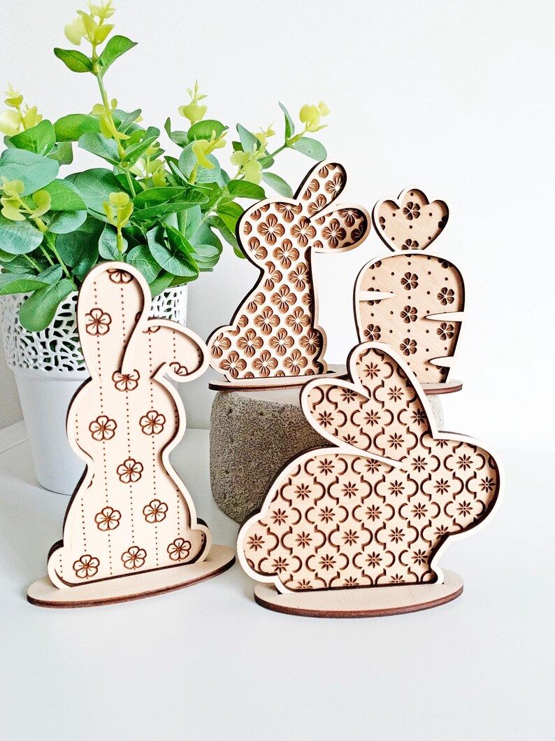 May include: Four wooden Easter bunny decorations with different floral patterns. The bunnies are standing on a white surface.