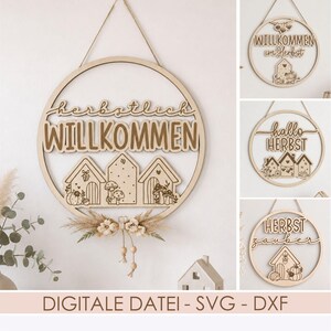Peut inclure: Une enseigne murale circulaire en bois avec le texte "herbstlich WILLKOMMEN" au-dessus de trois silhouettes de maisons décorées de champignons et de citrouilles. L'enseigne comprend une cordelette et des fleurs séchées à la base.
