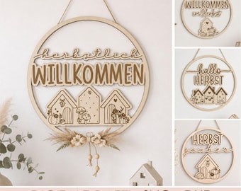 May include: A circular wooden wall sign featuring the text "herbstlich WILLKOMMEN" above three house silhouettes decorated with mushrooms and pumpkins. The sign includes a hanging string and a decorative arrangement of dried flowers at the base.
