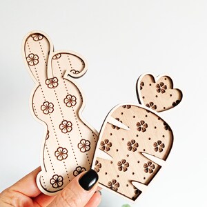 May include: Two wooden cutouts, a bunny and a carrot, both with a floral pattern. The bunny is brown and the carrot is orange.