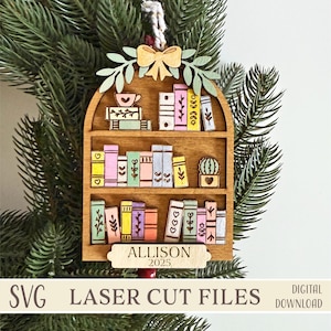 May include: Wooden bookshelf ornament featuring colourful books, a teacup, and a cactus. The ornament includes the name "ALLISON" and the year "2025". The text "SVG LASER CUT FILES" and "DIGITAL DOWNLOAD" are also present.