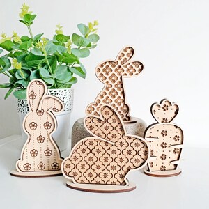 May include: Three wooden bunny figurines with a floral pattern. The bunnies are standing on a white surface.