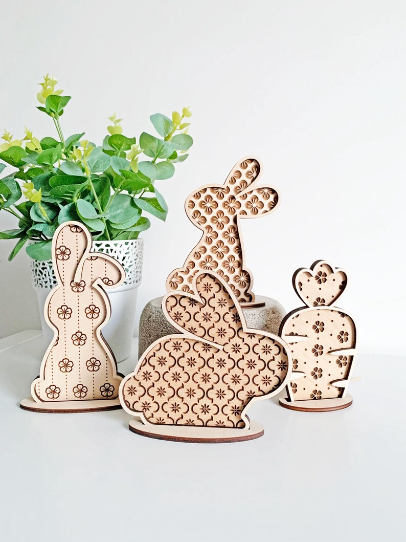 May include: Three wooden bunny figurines with a floral pattern. The bunnies are standing on a white surface.