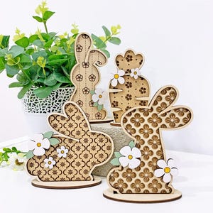 May include: Three wooden Easter bunny decorations with a floral pattern. The bunnies are standing on a white surface.