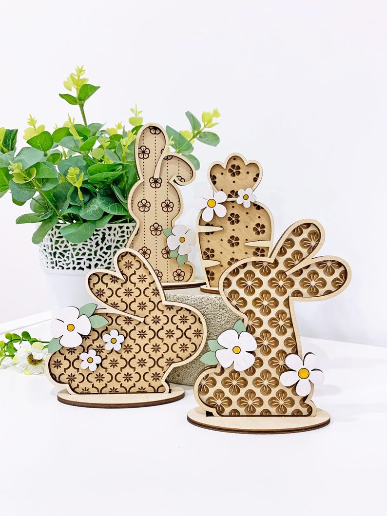 May include: Three wooden Easter bunny decorations with a floral pattern. The bunnies are standing on a white surface.