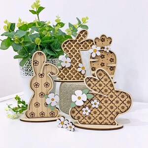 May include: Four wooden bunny and cactus decorations with white flowers. The bunnies have a patterned design and the cactus has a floral pattern.