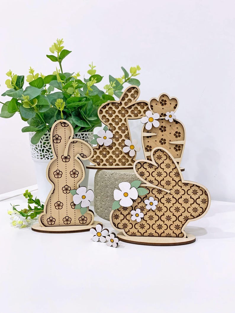 May include: Four wooden bunny and cactus decorations with white flowers. The bunnies have a patterned design and the cactus has a floral pattern.