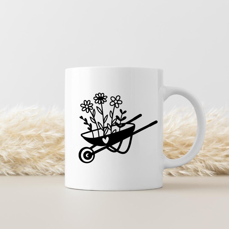 May include: White ceramic mug featuring a black illustration of a wheelbarrow filled with flowers and a heart. The wheelbarrow design is simple and elegant, perfect for gardening enthusiasts. The mug has a curved handle.