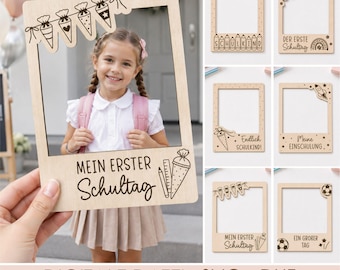Può includere: Una cornice portafoto in legno chiaro con disegni tagliati al laser a tema primo giorno di scuola, inclusi testi come 'MEIN ERSTER Schultag' e varie icone scolastiche come coni, matite e stelle per servizi fotografici.
