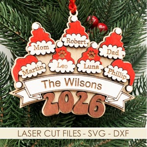 May include: A wooden Christmas ornament featuring six red Santa hats with white trim, each engraved with names including Mom, Robert, Dad, Martin, Leo, and Phillip. A central banner reads The Wilsons above the large wooden numbers 2026.