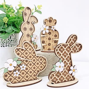 May include: Four wooden bunny and flower decorations with a geometric pattern. The bunnies are brown with white flowers and green leaves. The flower is brown with white flowers.