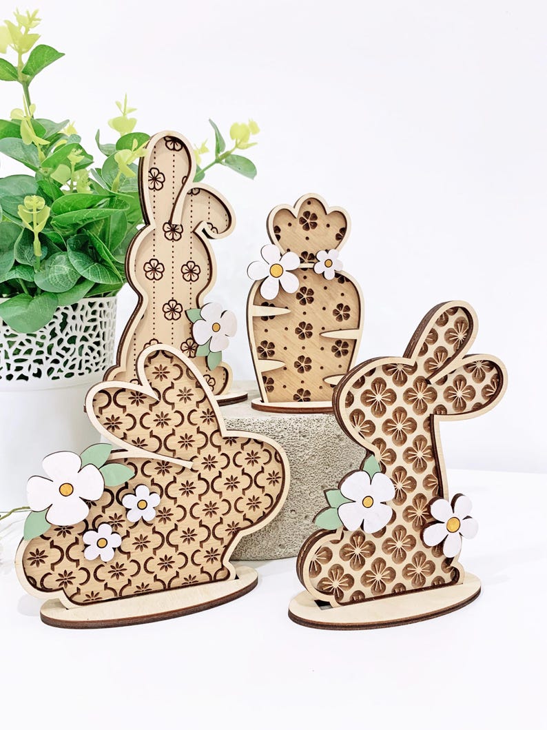 May include: Four wooden bunny and flower decorations with a geometric pattern. The bunnies are brown with white flowers and green leaves. The flower is brown with white flowers.