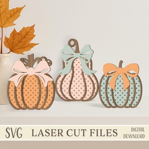 May include: Three wooden pumpkin decorations with polka dots and bows in pastel colors. The pumpkins are orange, pink, and teal, with bows in matching or contrasting shades. The image includes the text "SVG LASER CUT FILES DIGITAL DOWNLOAD."