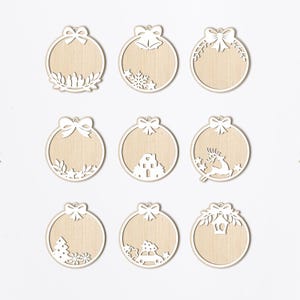 May include: Nine white wooden Christmas ornament cutouts with different designs. The ornaments are round and have a hole at the top for hanging. The designs include a bow, bells, a house, a reindeer, a Christmas tree, a car, and a lantern.