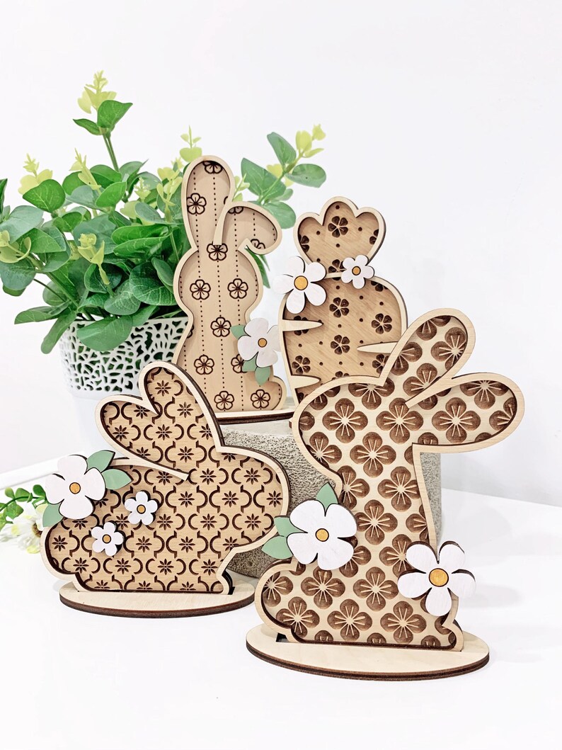 May include: Three wooden Easter bunny figurines with floral patterns and white flowers. The bunnies are standing on a wooden base.