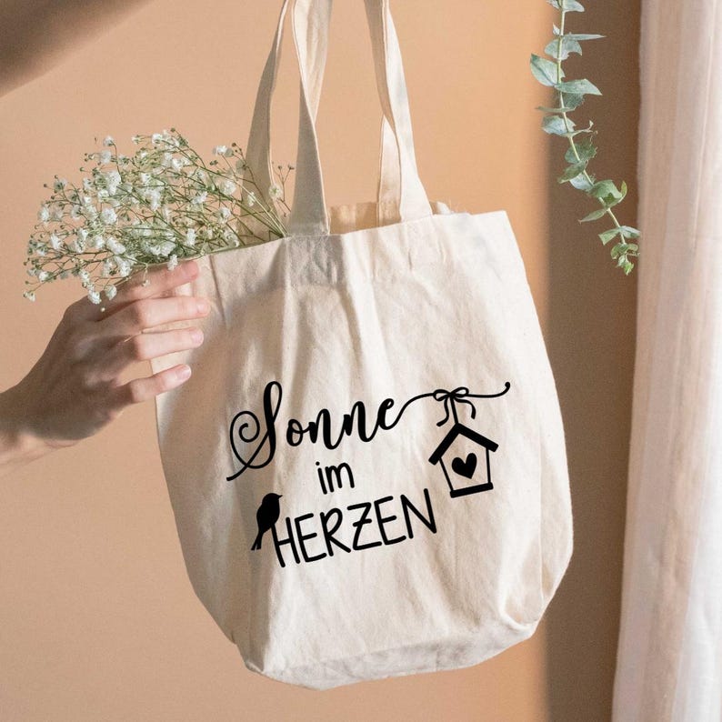 May include: A white ceramic mug with a black handle and the text "But First, Coffee" in a bold, black font. The mug is set against a blurred background, suggesting a cozy setting.