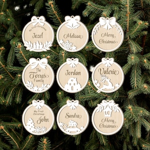 May include: Nine wooden Christmas baubles with various designs and names. The baubles feature a reindeer, a house, a car, a tree, bells, and a wreath. The names on the baubles include Jozef, Melissa, Merry Christmas, The Torres Family, Jordan, Valerie, John, Sandra, and Merry Christmas.