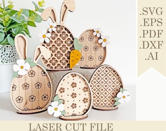 May include: Set of five laser cut wooden Easter eggs, each with a different patterned design. Two of the eggs have bunny ears. The eggs are decorated with white flowers and a small orange carrot.
