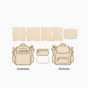 Puede incluir: Un kit de manualidades de madera clara con paneles planos y dos recortes en forma de mochila. La pieza frontal muestra el texto Endlich SCHULKIND! con ilustraciones de una regla y un cono. El conjunto incluye una peque&ntilde;a pieza rectangular.